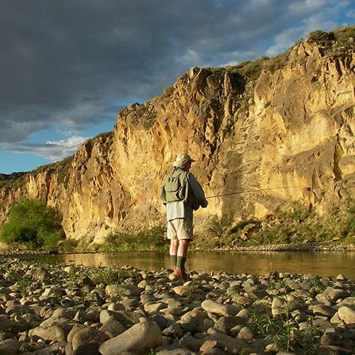 Expert fly fishing guide casting on the scenic Pichi Leufú River in Bariloche, Patagonia, Argentina. Experience world-class day fishing trips with a top-rated outfitter.