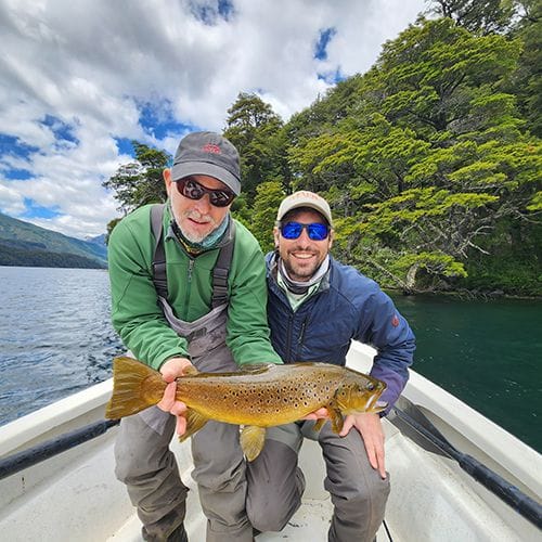 Angler and fishing guide showcasing a large brown trout caught on a fly fishing trip at Fonck Lake, Bariloche, Patagonia, Argentina, known for its big brook and brown trout and scenic full-day fishing charter